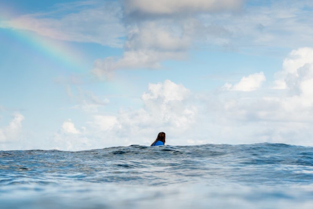 Surfer waiting in the ocean beneath a rainbow